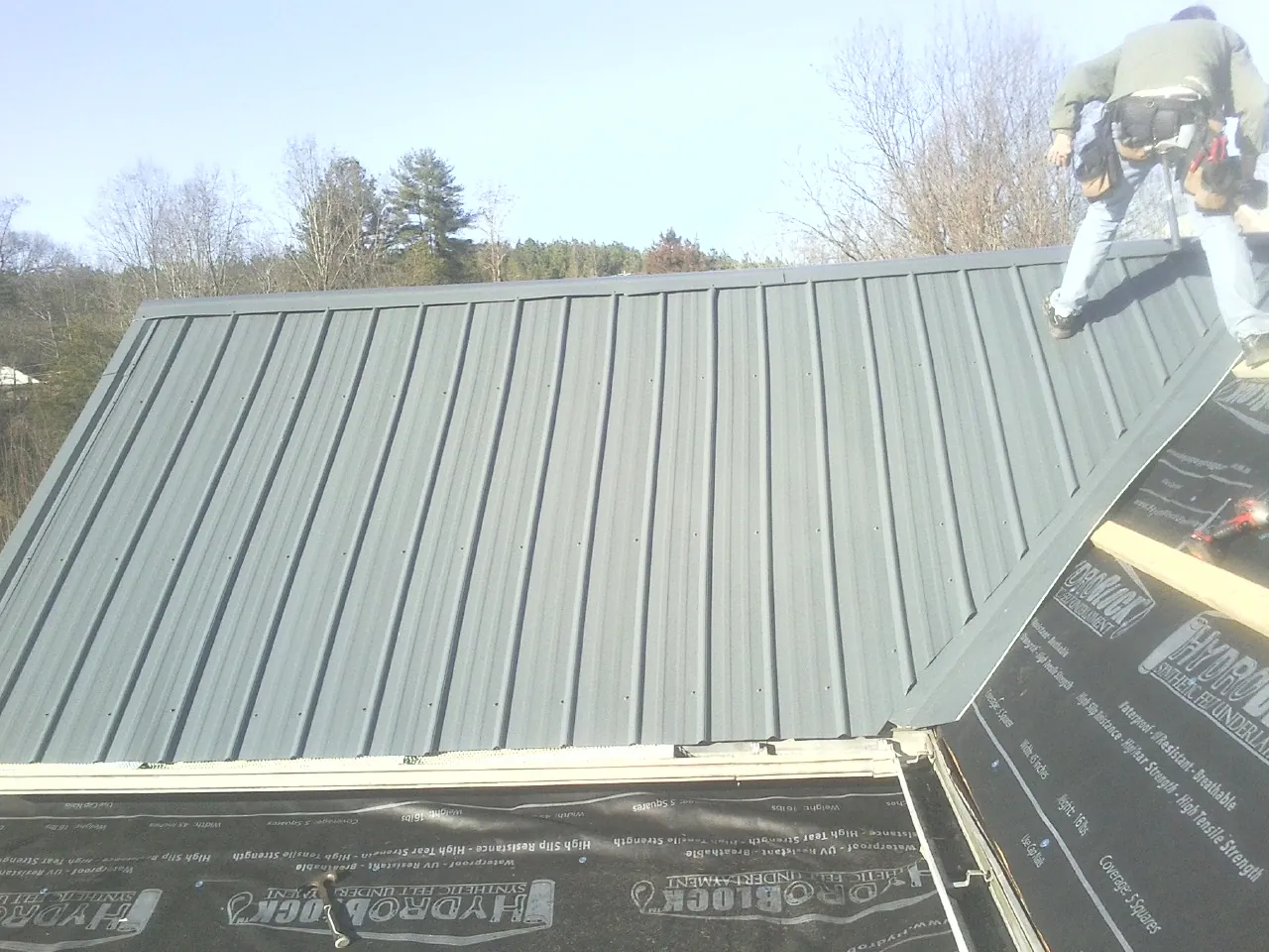Crew installing dark green standing seam panels over synthetic underlayment in Mc Caysville