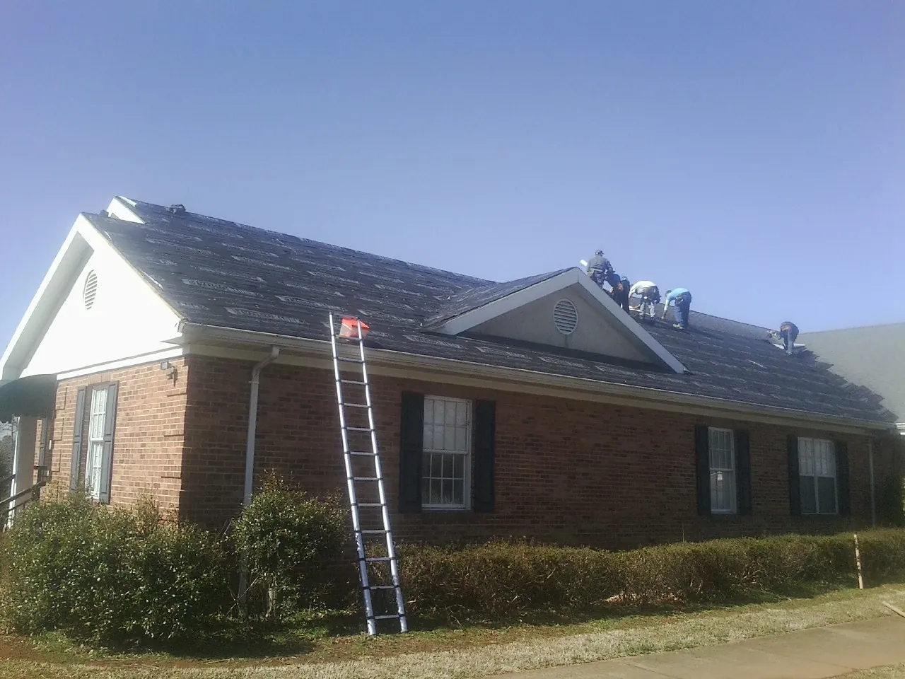 Crew tearing shingles off a brick ranch roof with a ladder set — Emergency Roof Repair work by our crew in Mc Caysville