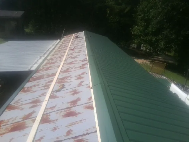 Old rusted panels beside newly installed green metal roofing — Wind Damage Roof Repair by Roofing Brothers in Mc Caysville