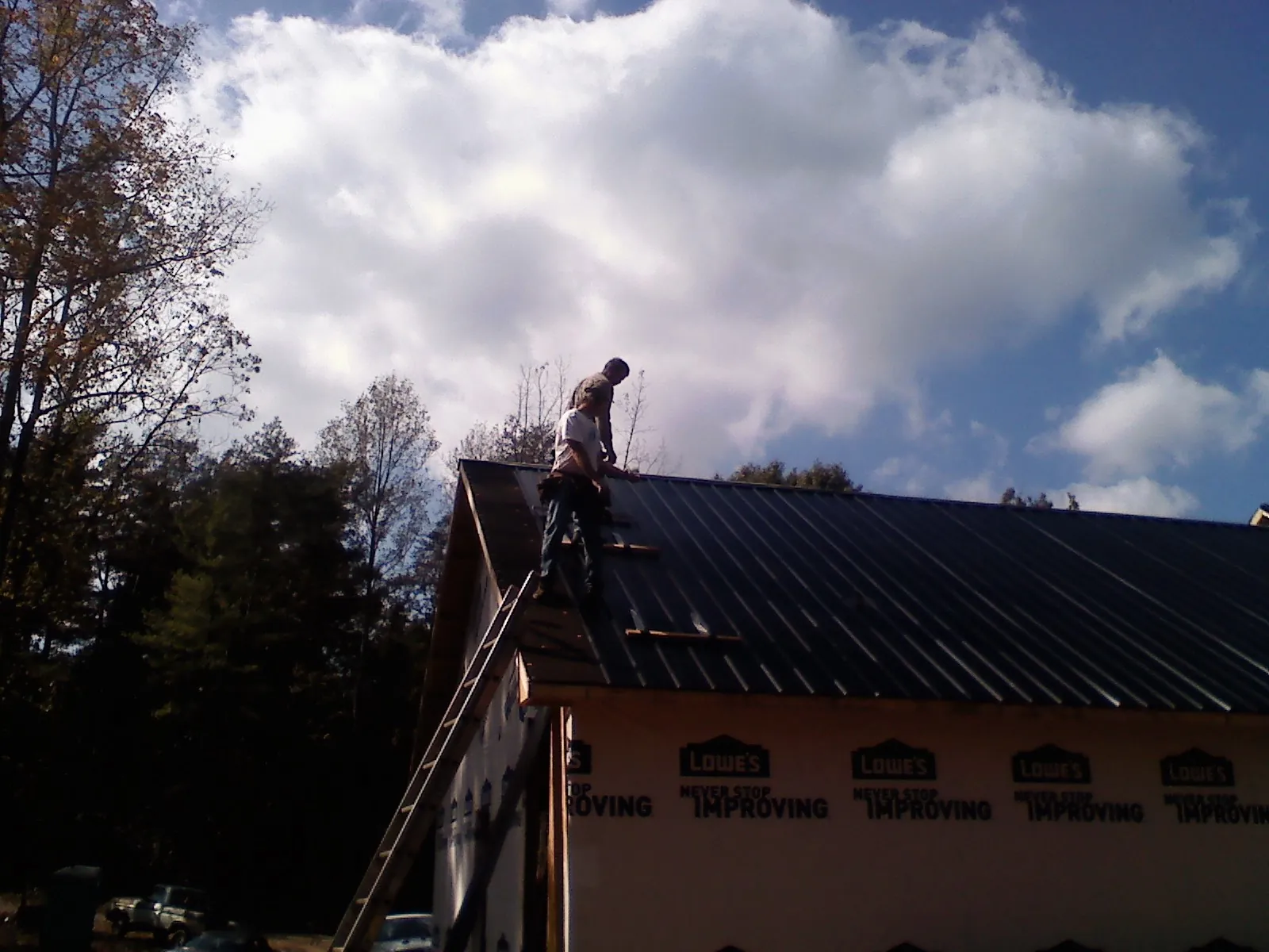 Roofer fastening dark metal panels high against a cloudy sky, from a Roof Inspection job in Mc Caysville