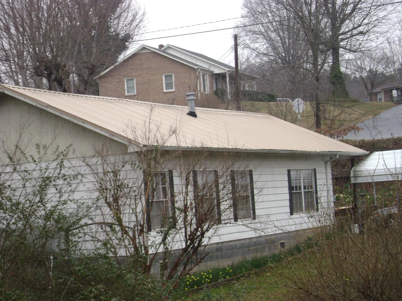 Tan metal roof on a white sided house set into a hillside — Commercial Roofing by Roofing Brothers in Mc Caysville